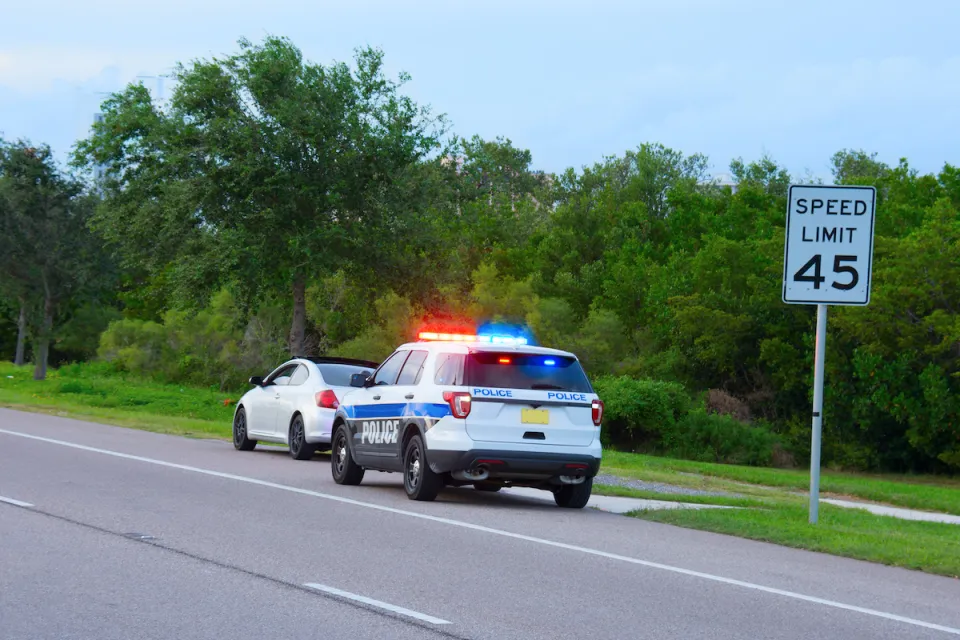 White and blue police SUV pulling over small white sedan in front of 45 mph speed limit sign.